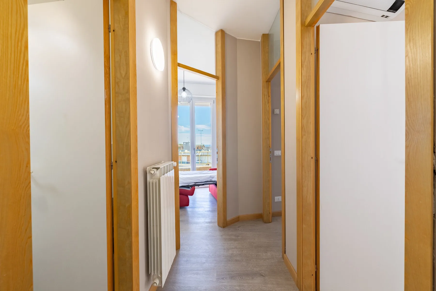 A narrow interior hallway with wood-trimmed doorways leads to a room with a window.