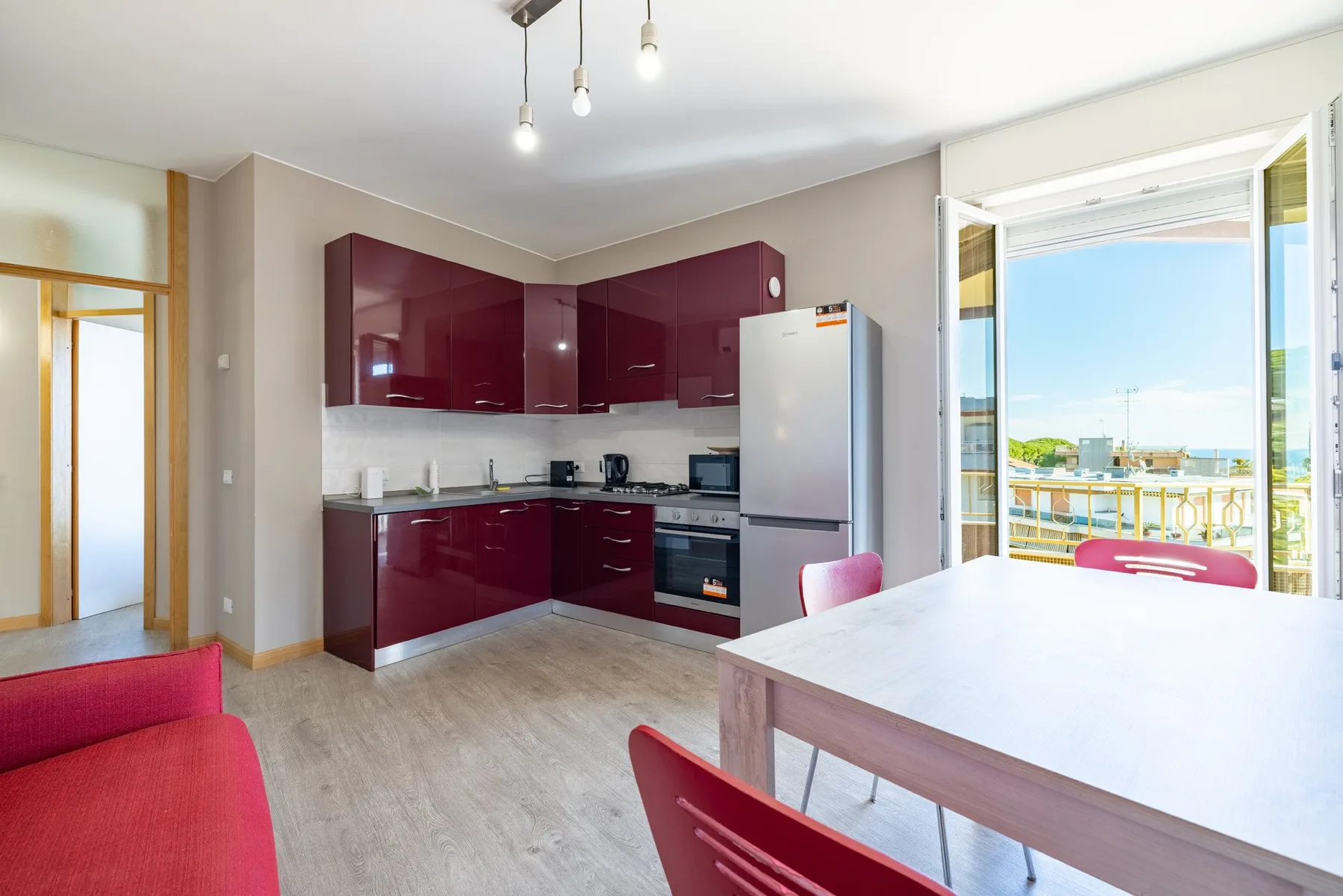 A modern kitchen with dark red cabinets opens onto a balcony.