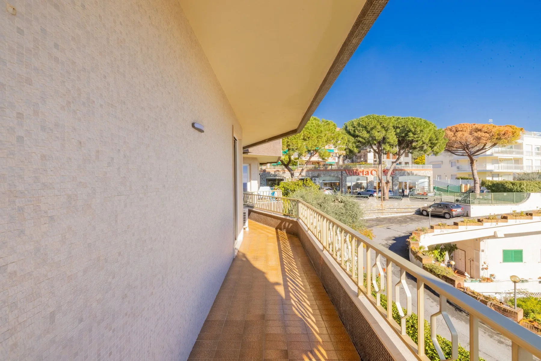 A covered balcony overlooks a tree-lined street and nearby buildings.