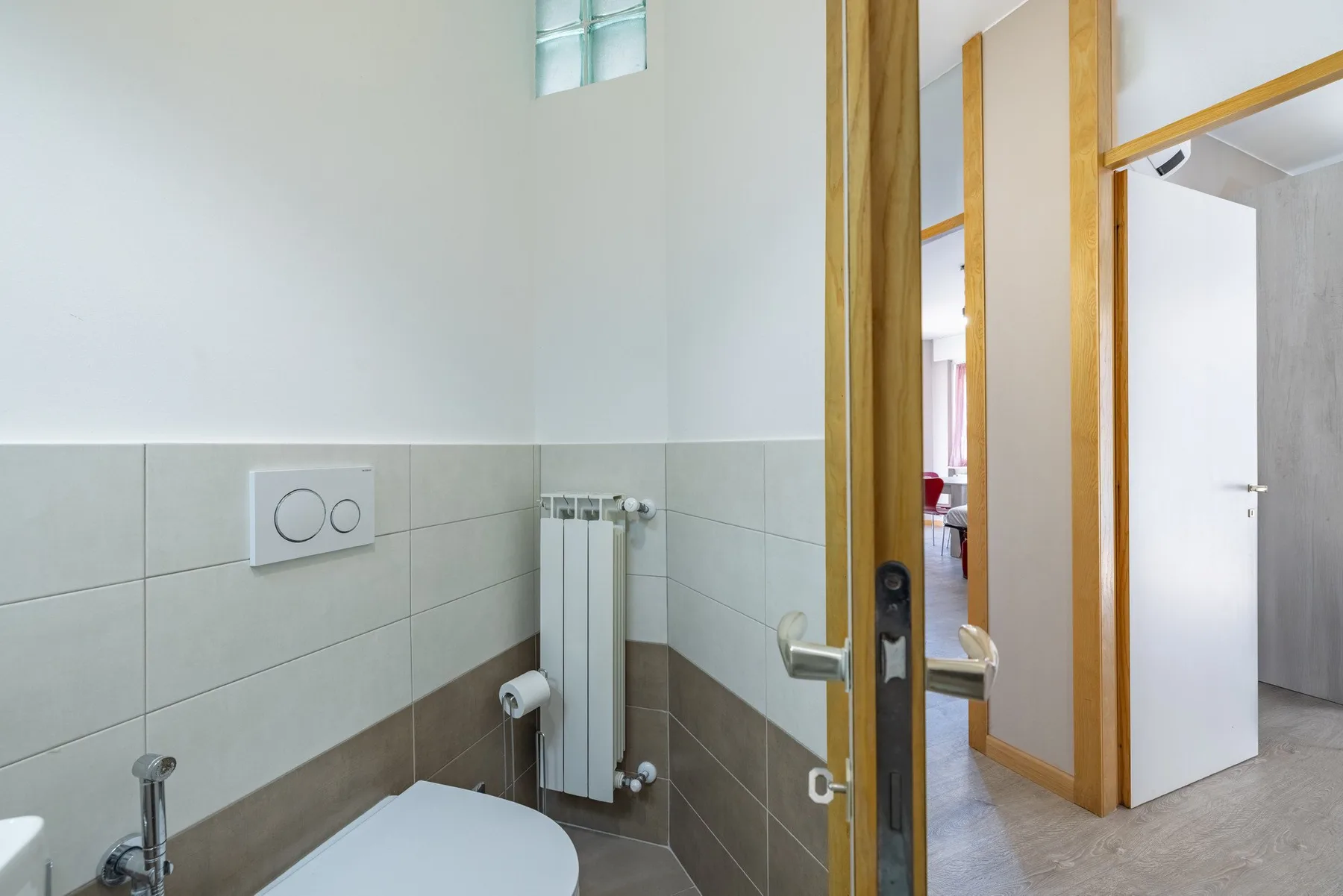 A bathroom with a toilet, wall-mounted radiator, and an open wooden door.