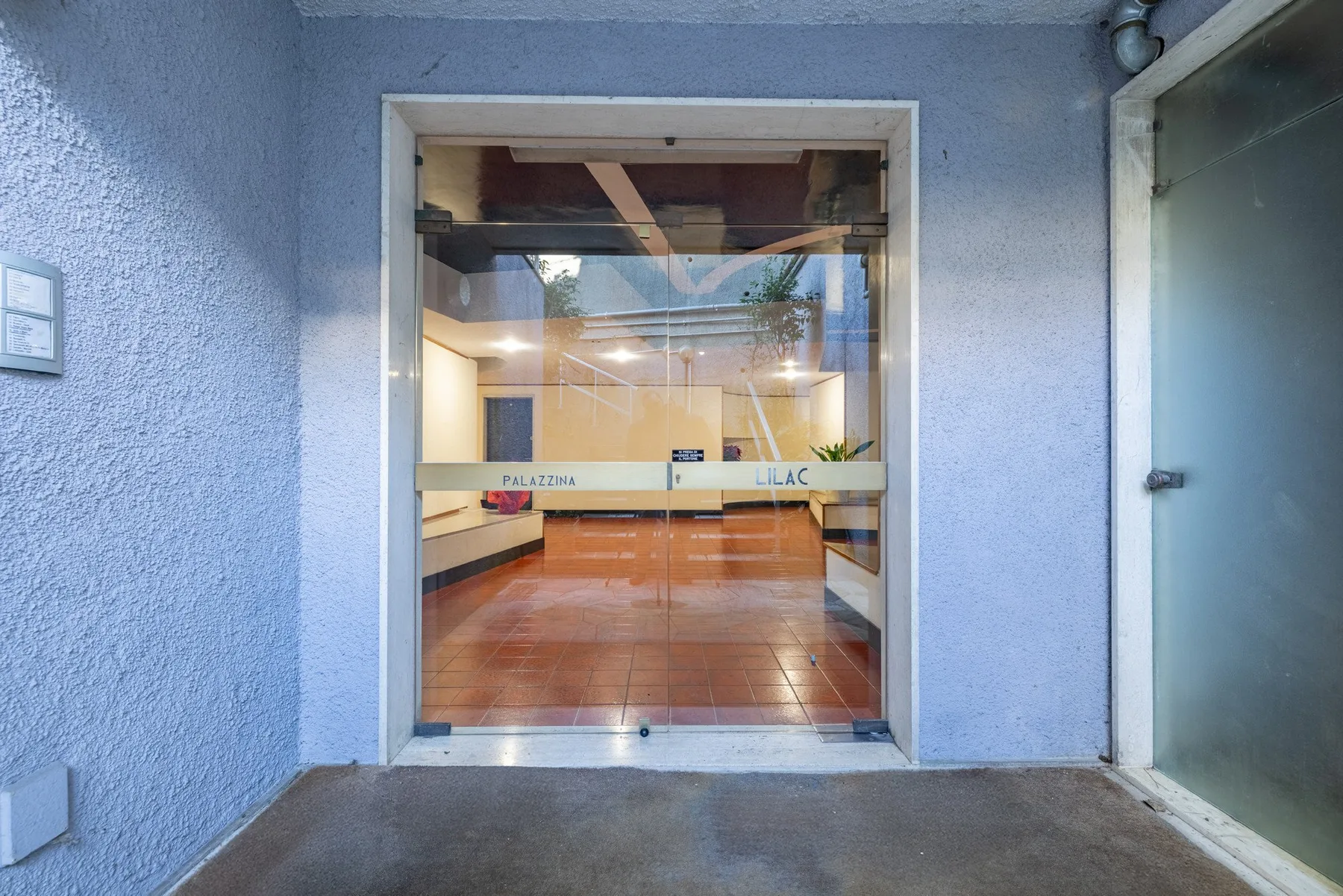 A glass entrance opens onto a bright lobby with tiled flooring.