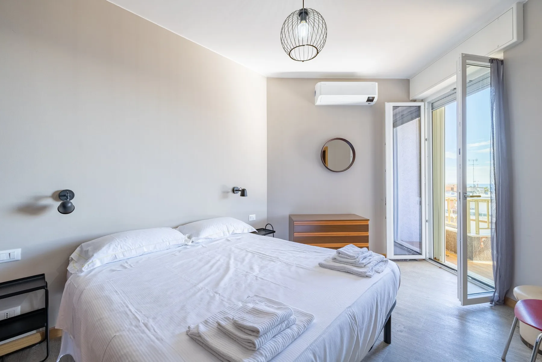 A bright bedroom with a neatly made bed and open balcony doors.
