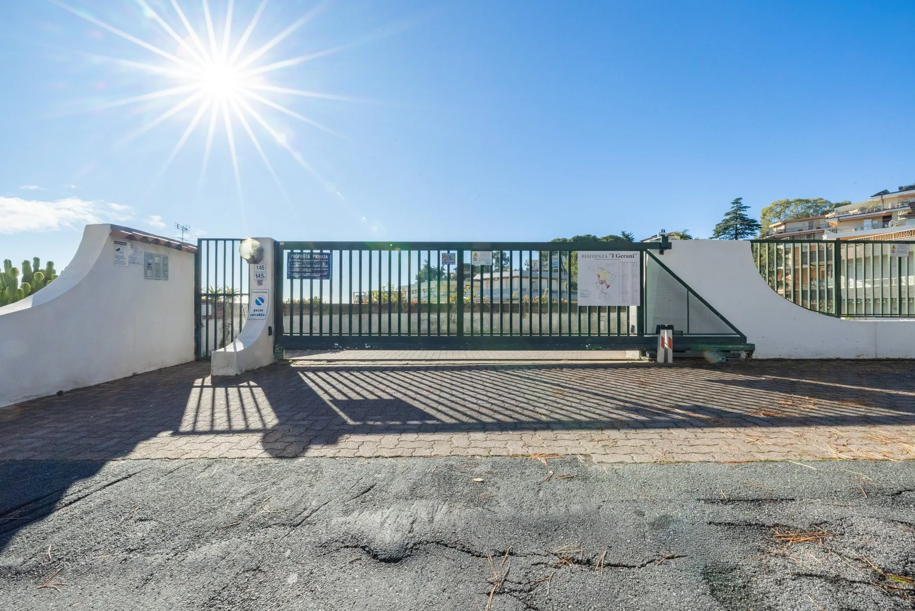 A gated entrance with a paved driveway beneath a bright blue sky.
