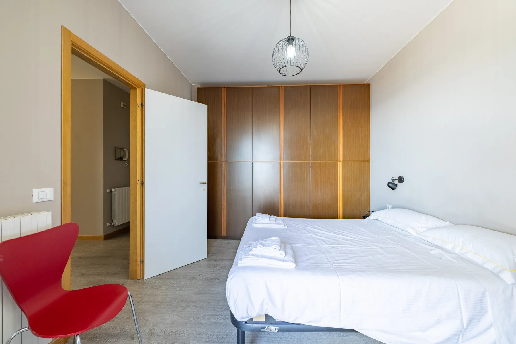 A bedroom with white bedding and a wood-paneled wall behind the bed.