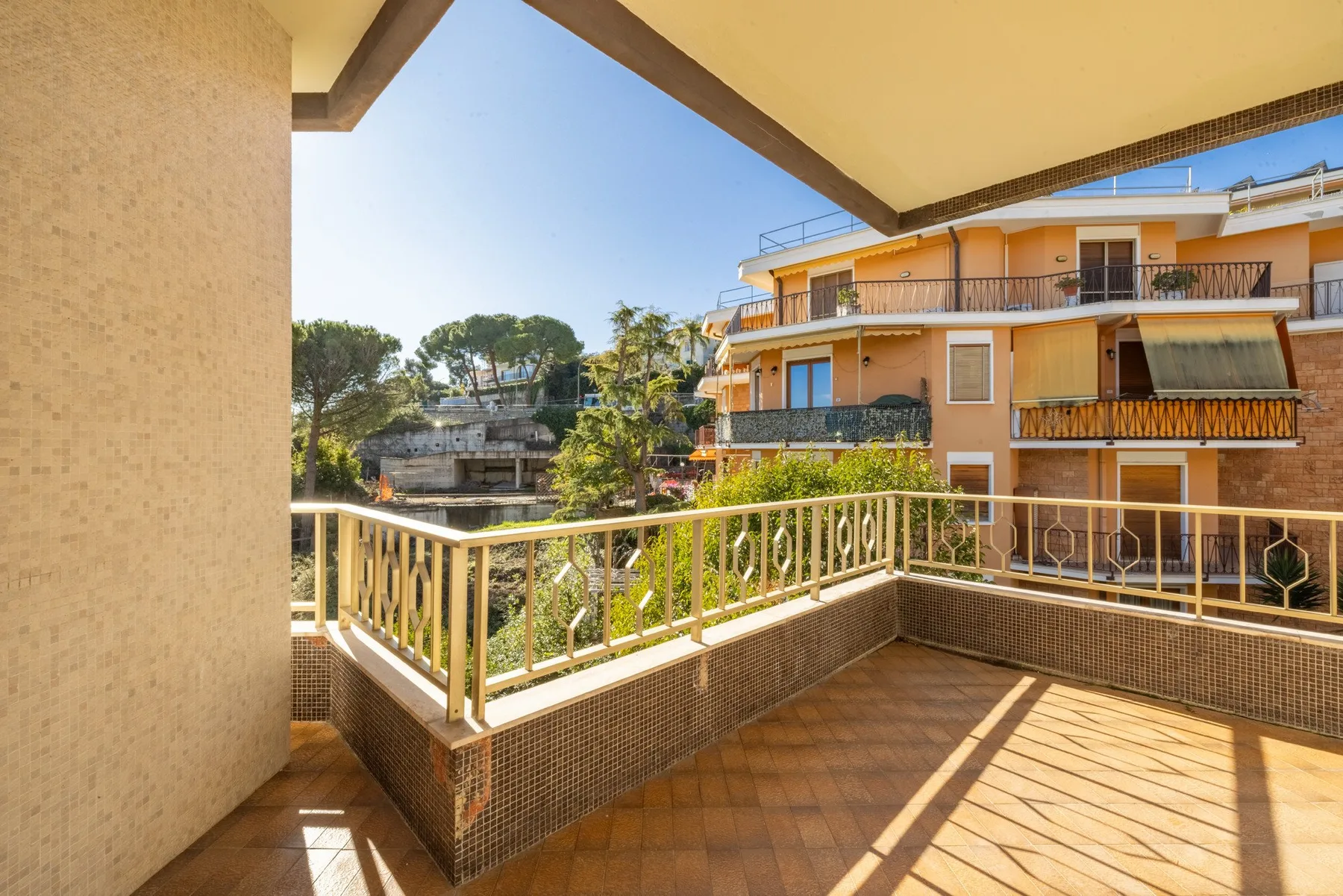 A sunlit balcony overlooks neighboring buildings and trees.