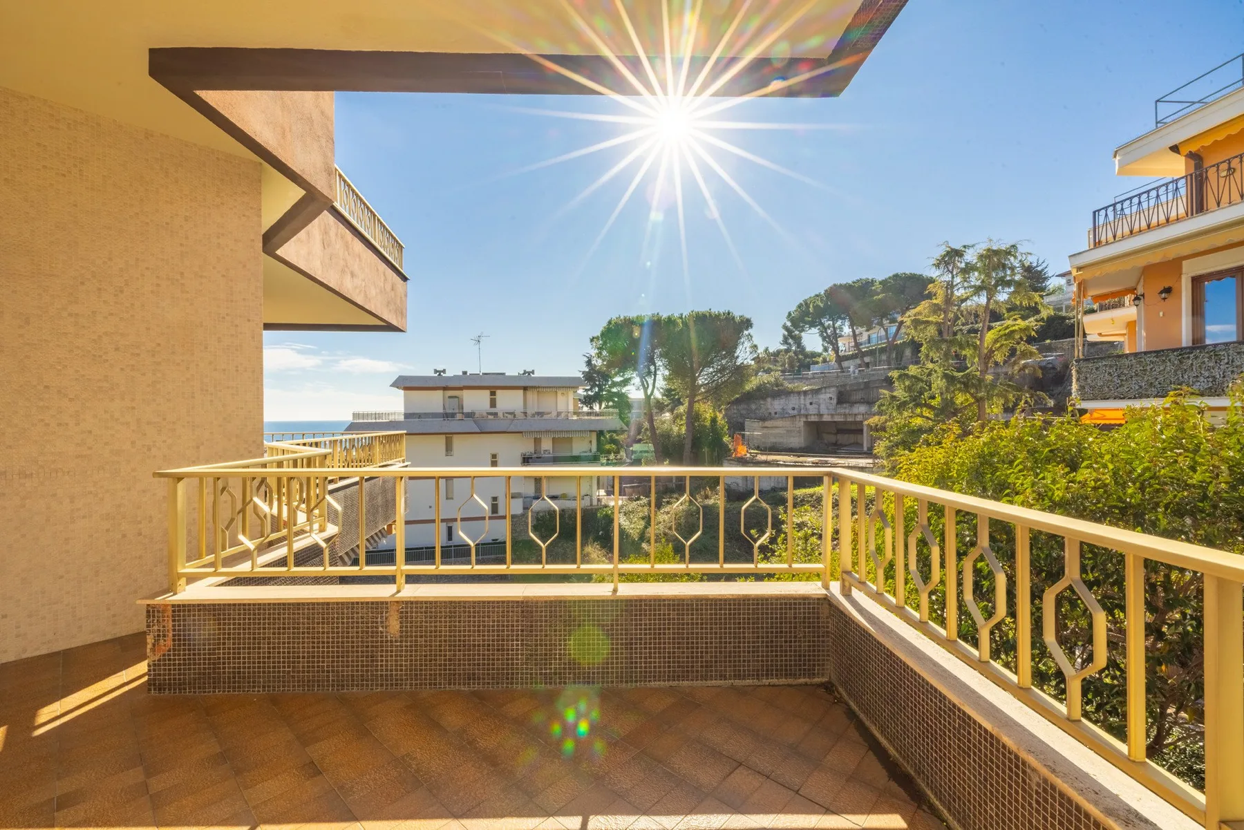 A sunlit balcony overlooks nearby buildings and a glimpse of the sea.