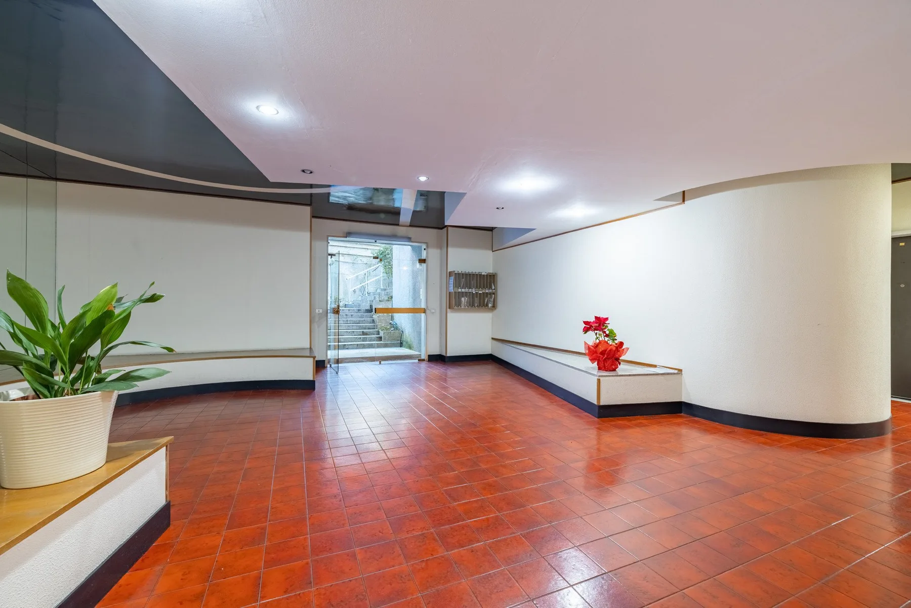 A spacious lobby with a tiled floor, a potted plant, and a glass entrance.