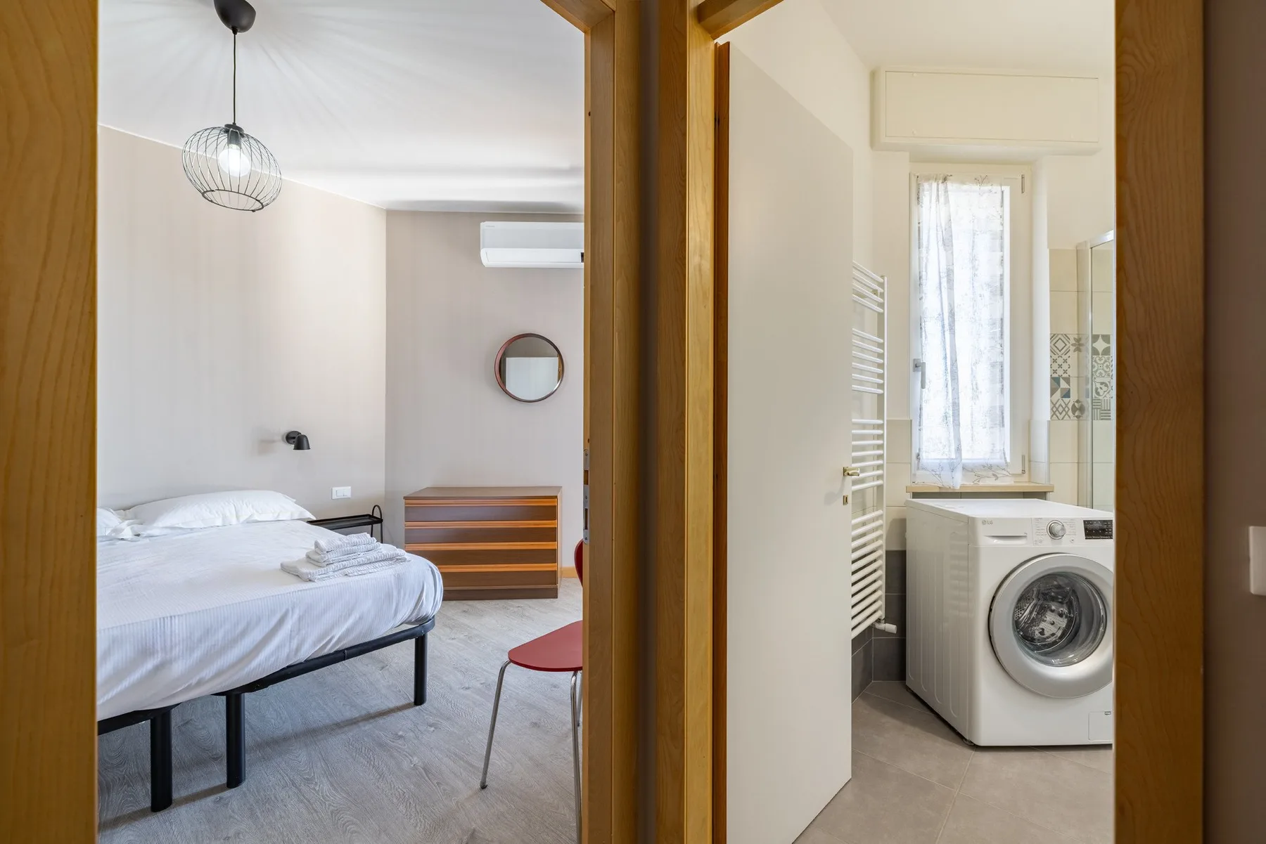 A bedroom and bathroom are visible through adjoining doorways, with a bed and washing machine.