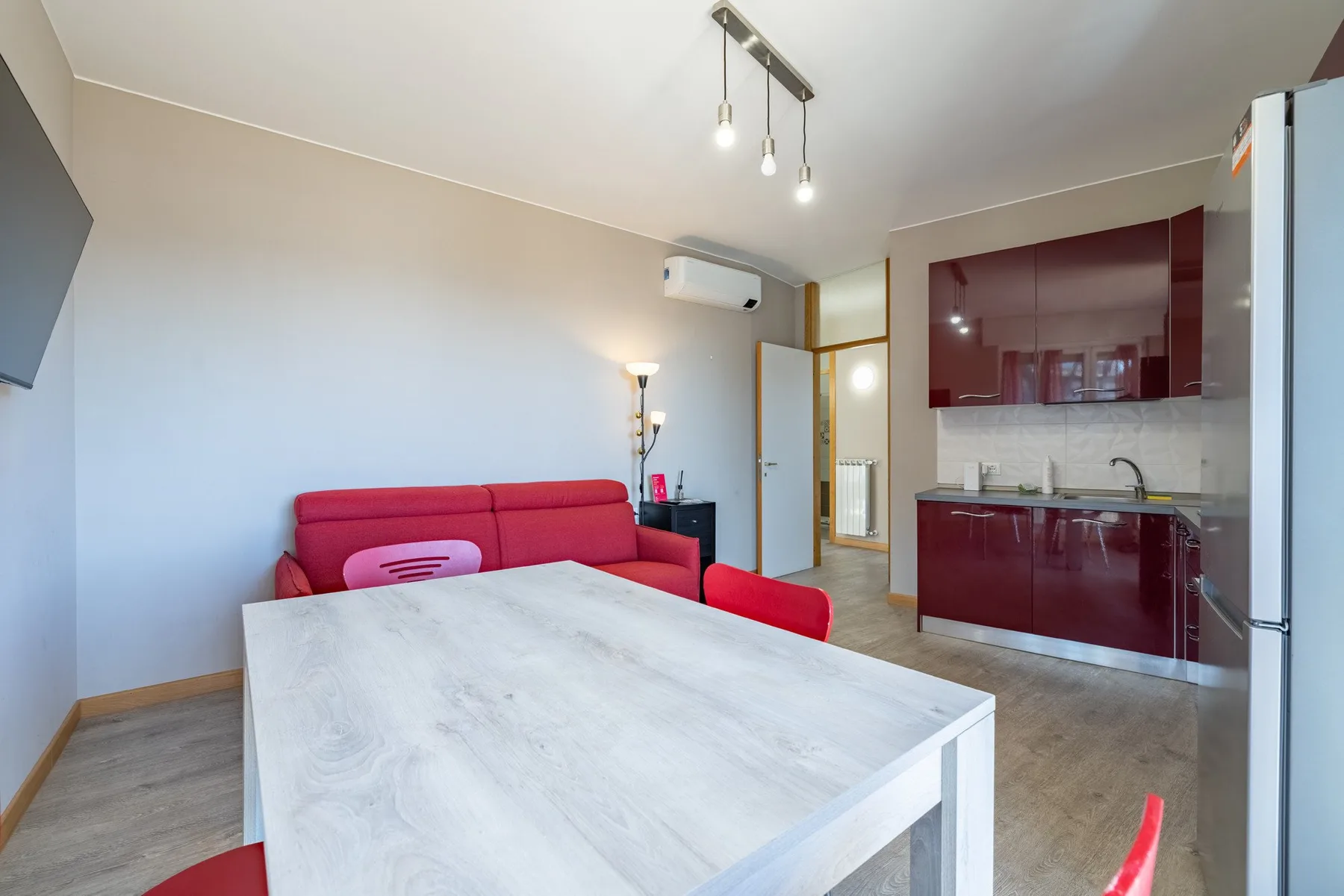 A bright living and kitchen area with a red sofa and white table.