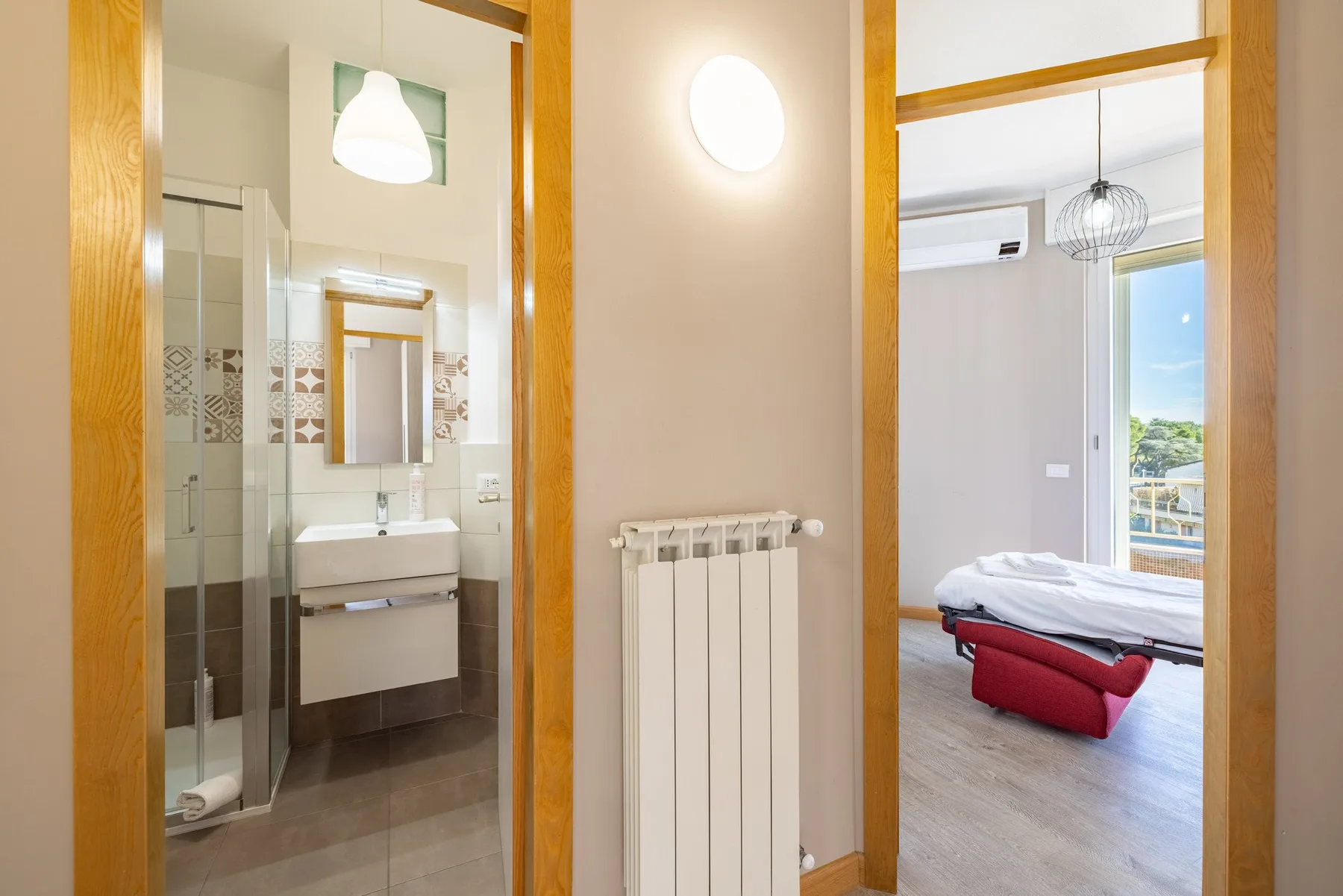 A hallway opens onto a bathroom with a sink and a bedroom with a bed.
