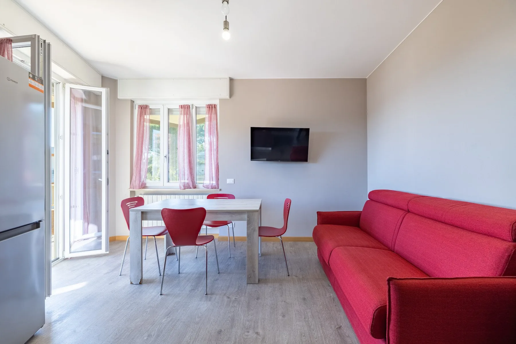 A living and dining area with a red sofa, table, and wall-mounted television.