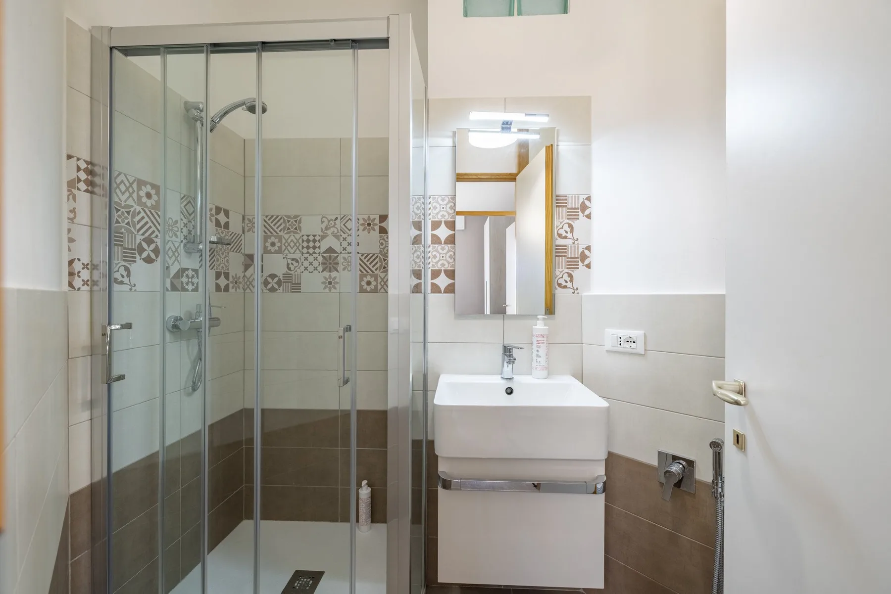 A tiled bathroom with a glass shower and wall-mounted sink.