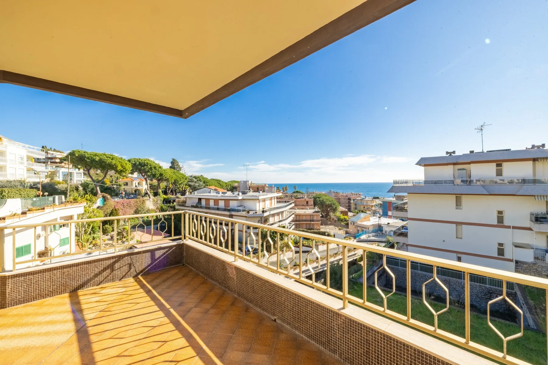 A sunlit balcony overlooks nearby buildings and the sea.