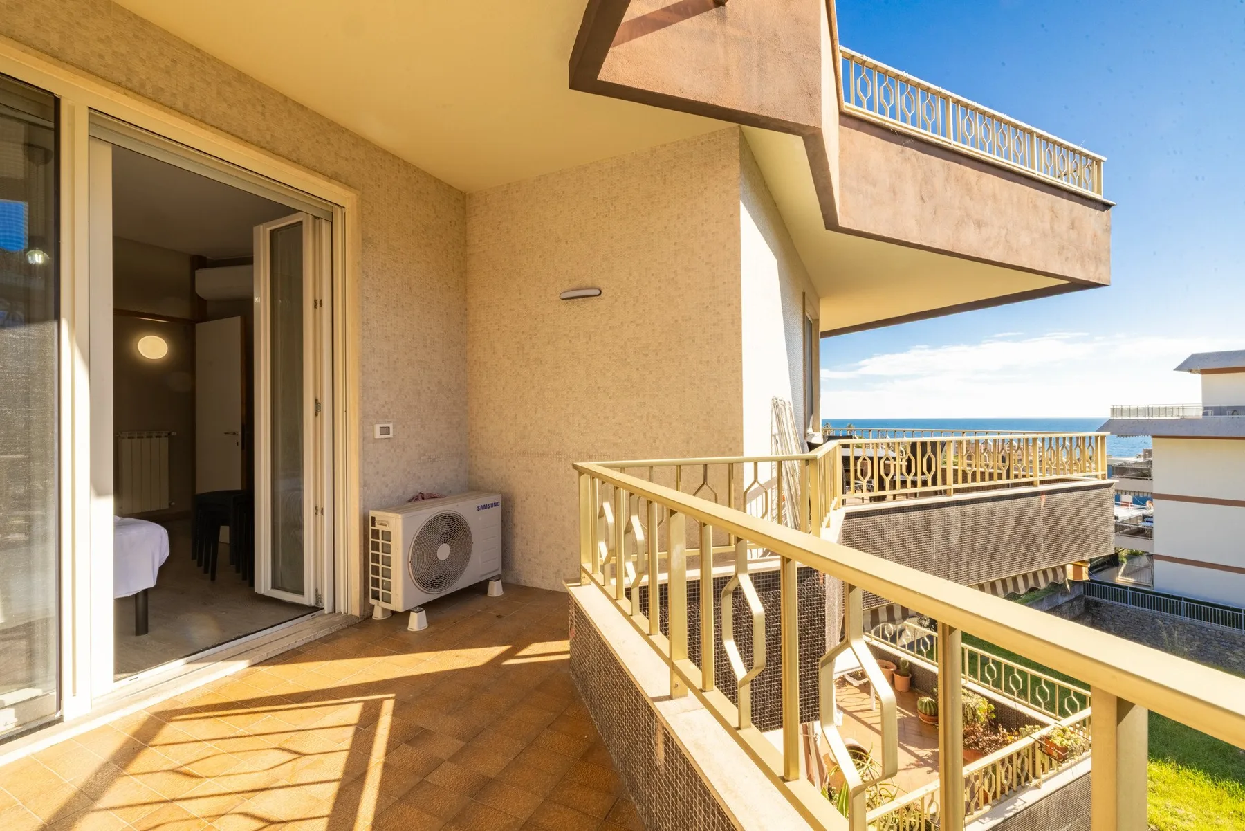 A sunlit balcony with railings and open views of neighboring buildings.