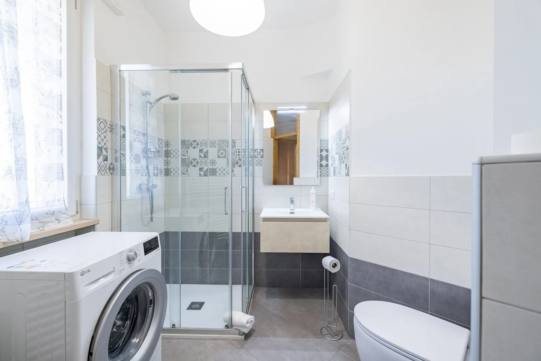 A bright bathroom with a glass shower, washing machine, and toilet.