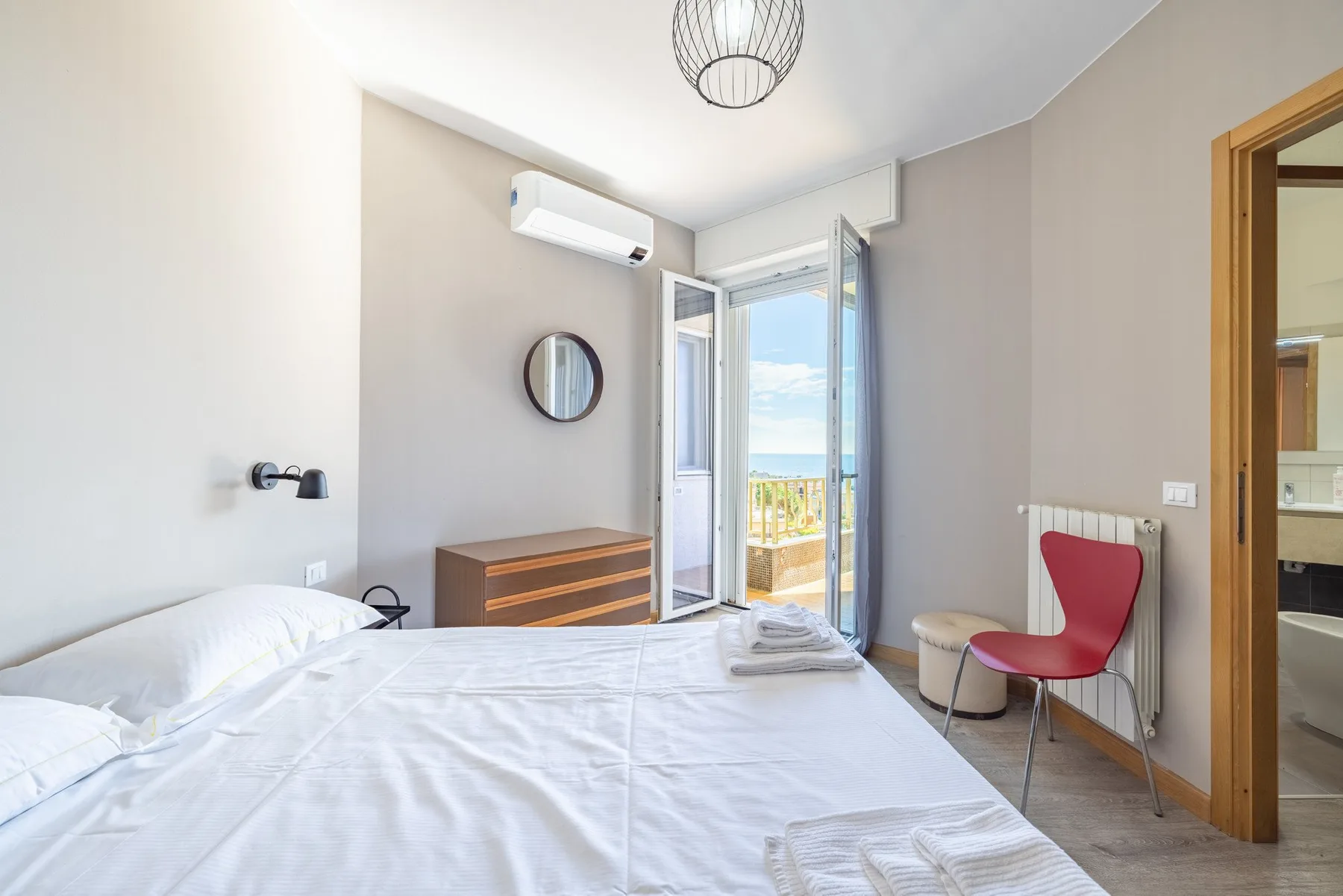 A bright bedroom with a bed and an open balcony door overlooking the sea.