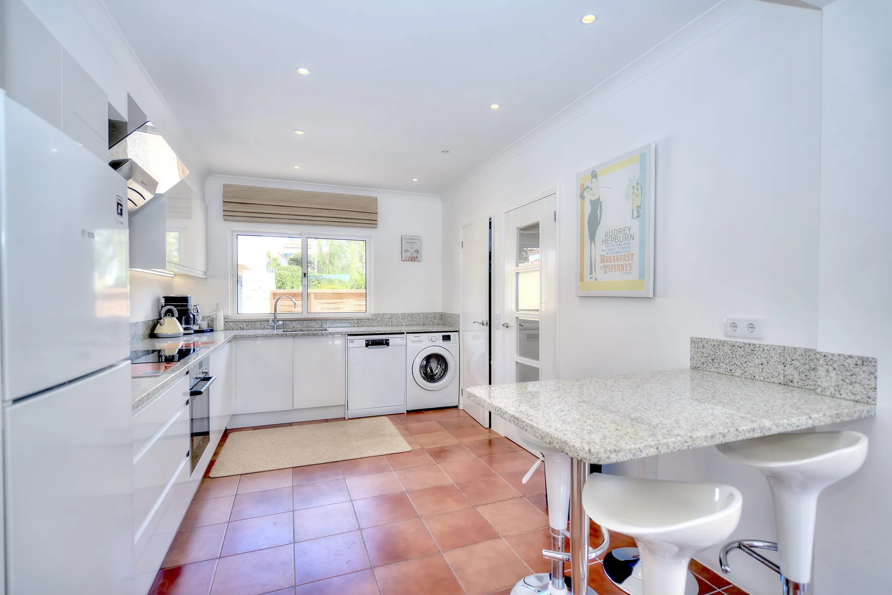 A bright kitchen with white cabinets, a window, and a breakfast counter.