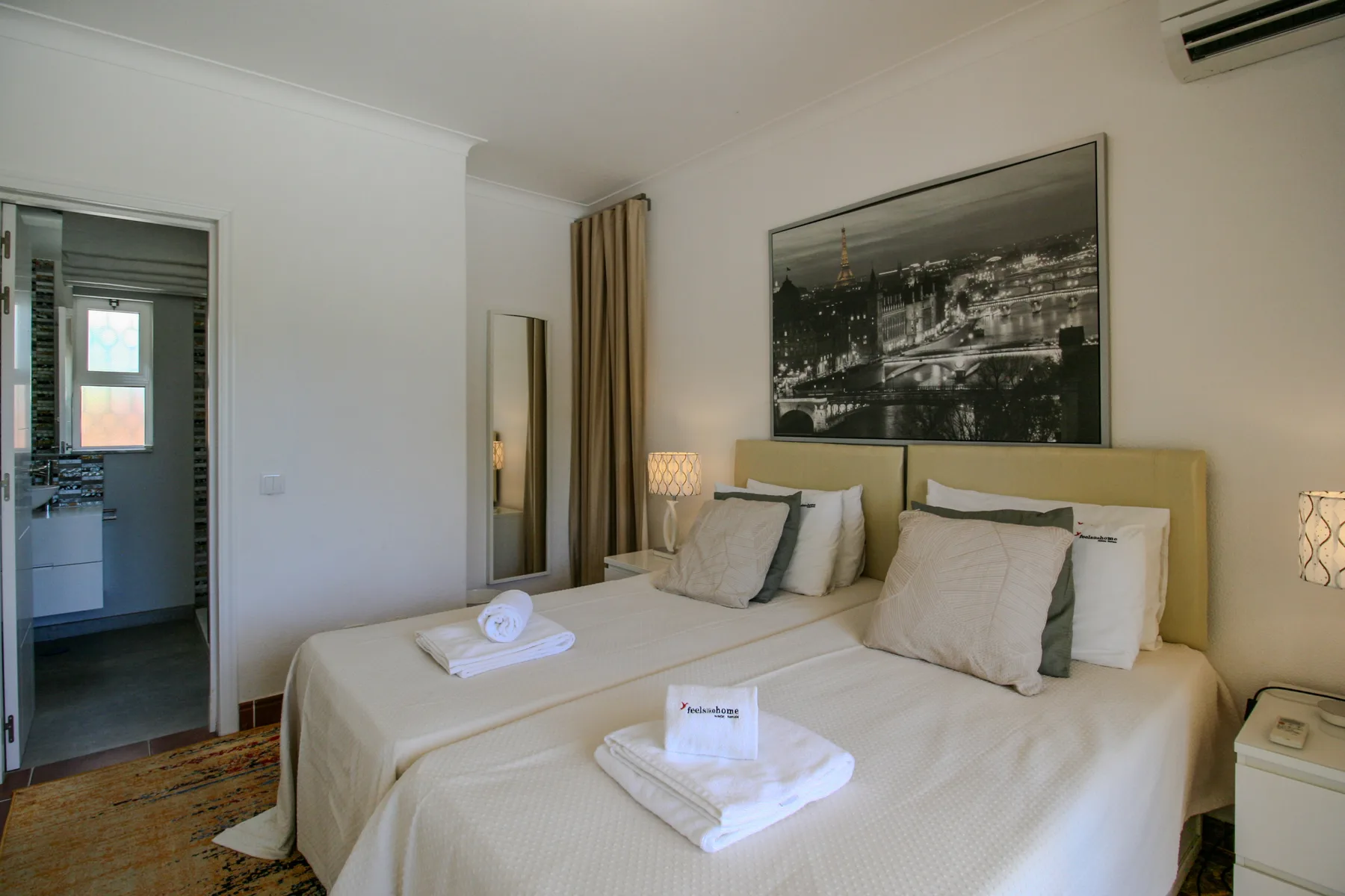 A bedroom with a double bed, folded towels, and a large framed picture above the headboard.
