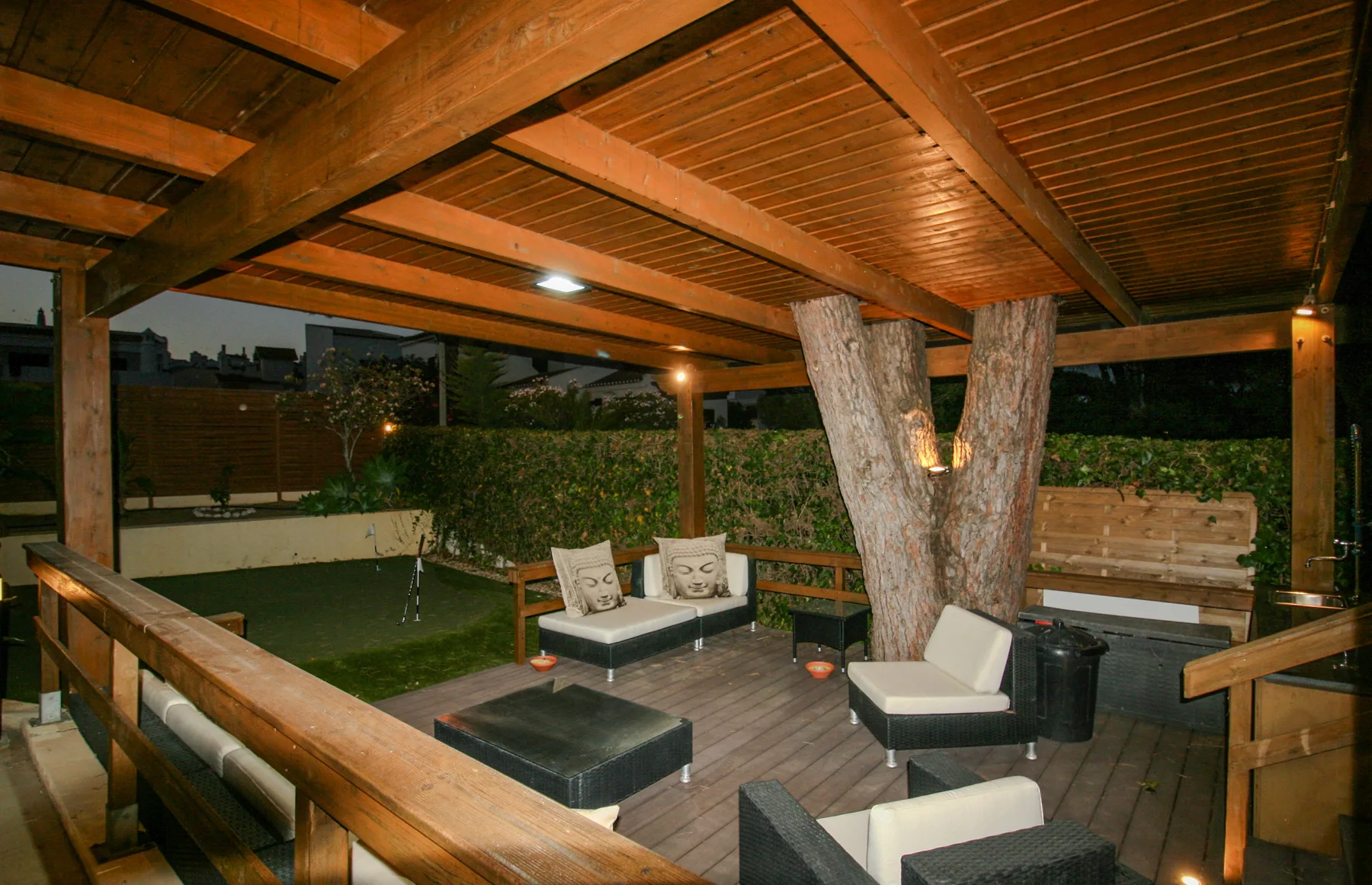 A covered outdoor seating area with wooden beams overlooks a small garden.