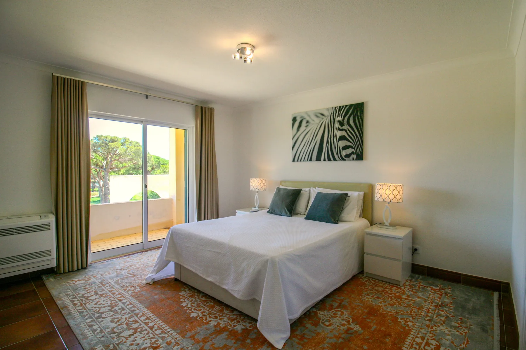 A bedroom with a bed, bedside tables, and sliding glass doors opening onto a balcony.