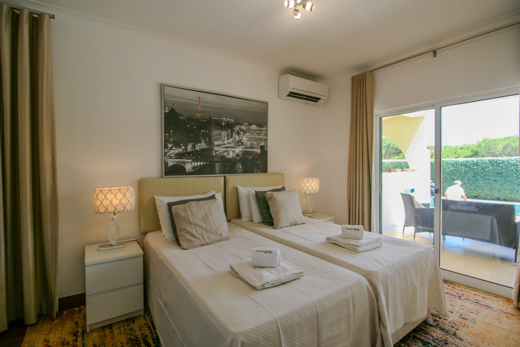 A bedroom with two beds, bedside tables, and sliding glass doors to a balcony.