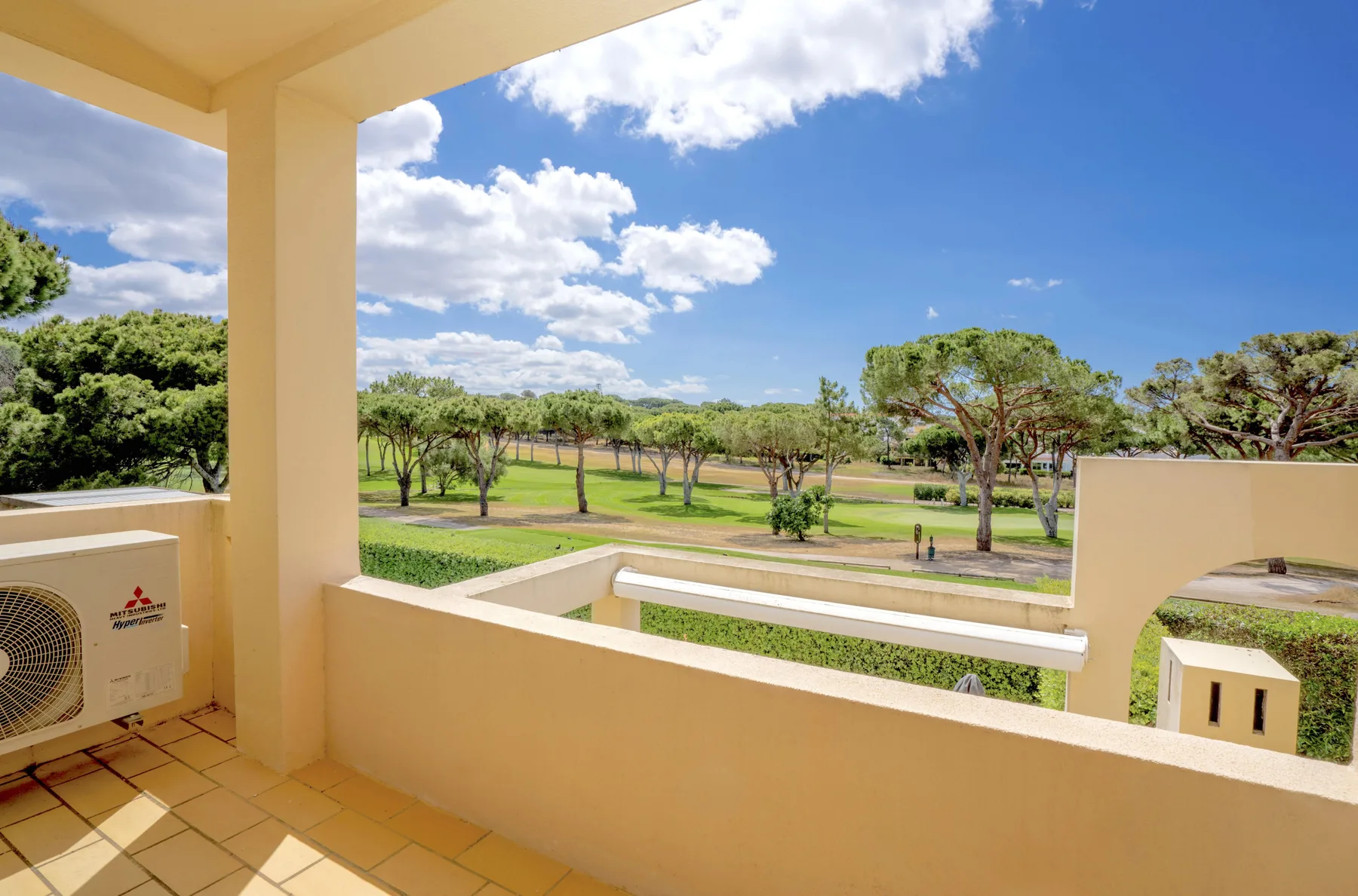 A covered terrace overlooks a landscaped green space with trees.