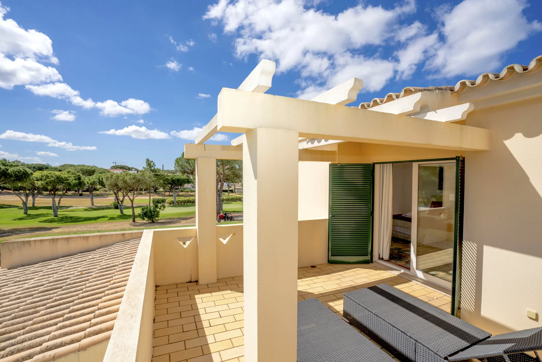 A sunny rooftop terrace with outdoor seating overlooks a green landscape.
