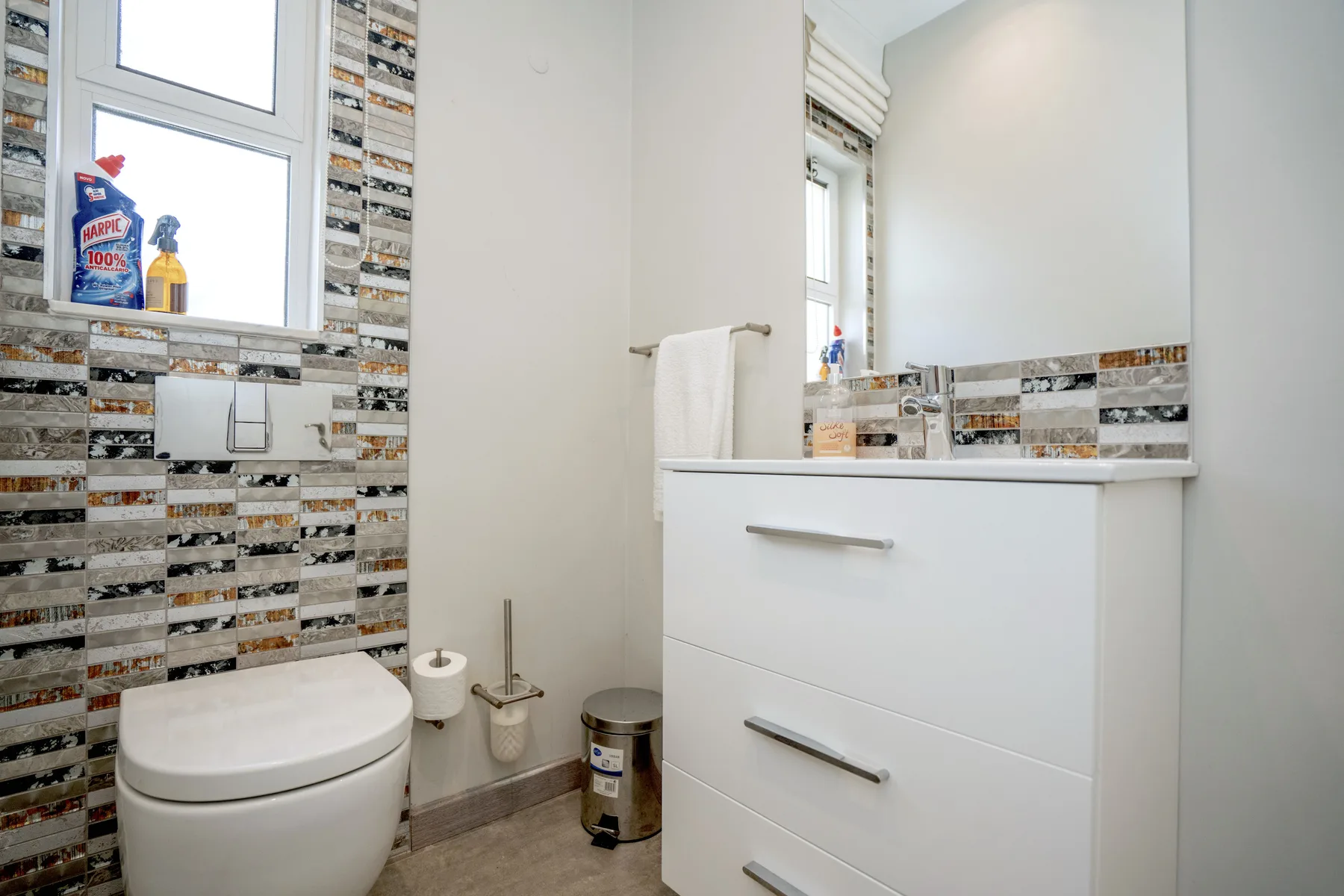A bathroom with a bathtub, sink vanity, toilet, and patterned wall tiles.