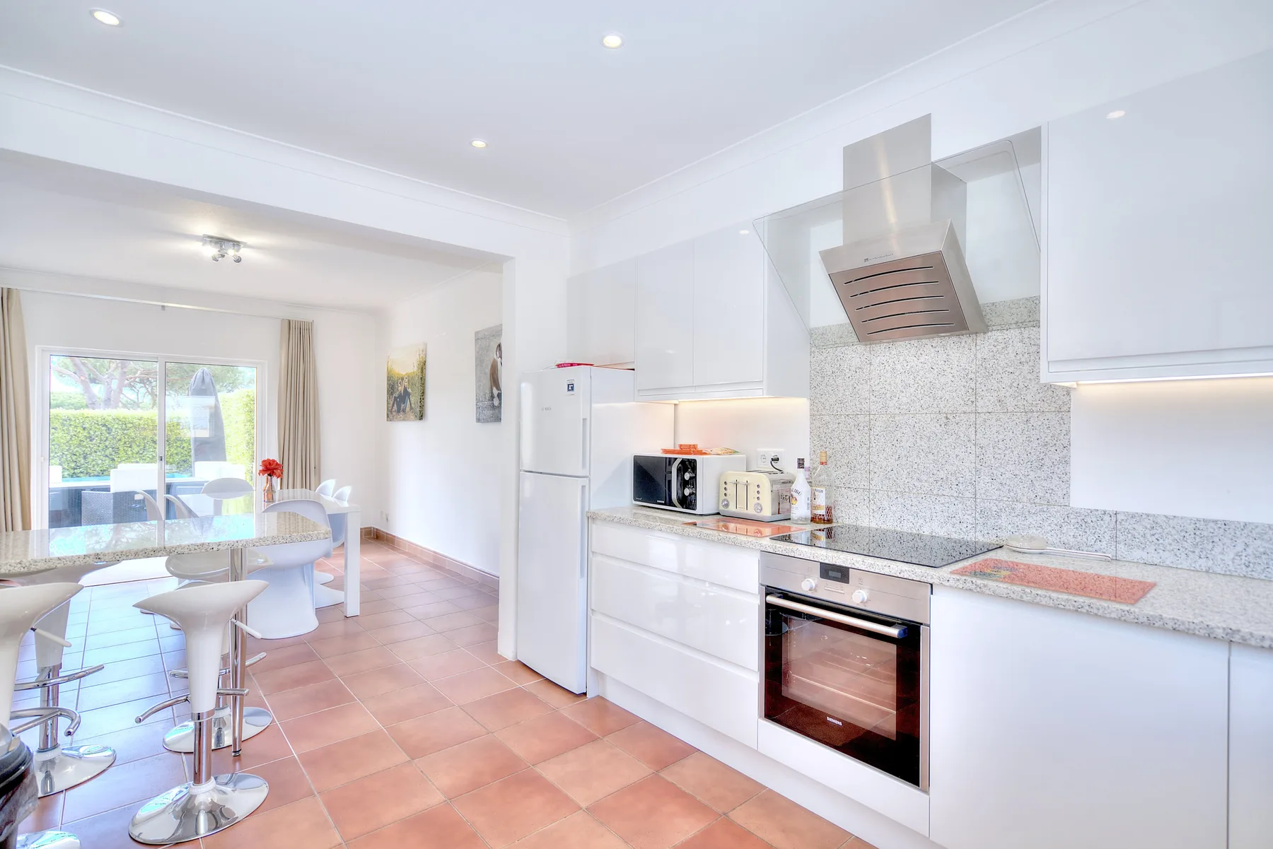 A bright kitchen opens into a dining area with a table and chairs.