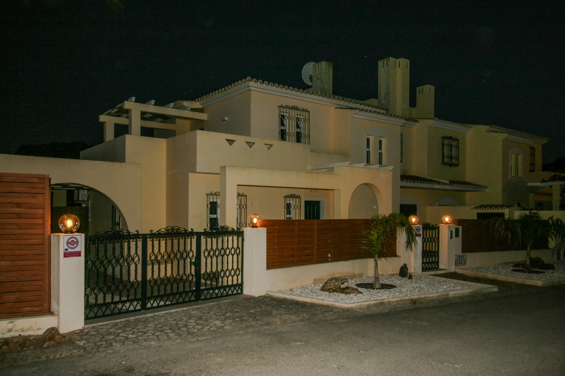 A large residence is shown at night behind a decorative metal gate.