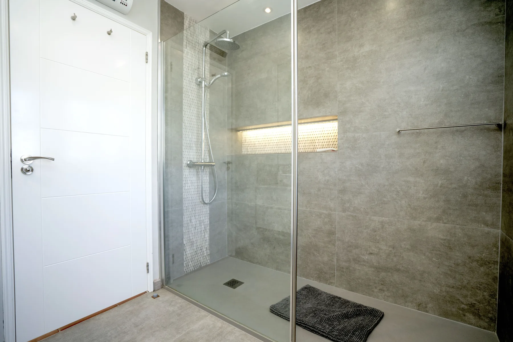 A modern bathroom with a glass shower and a recessed illuminated shelf.
