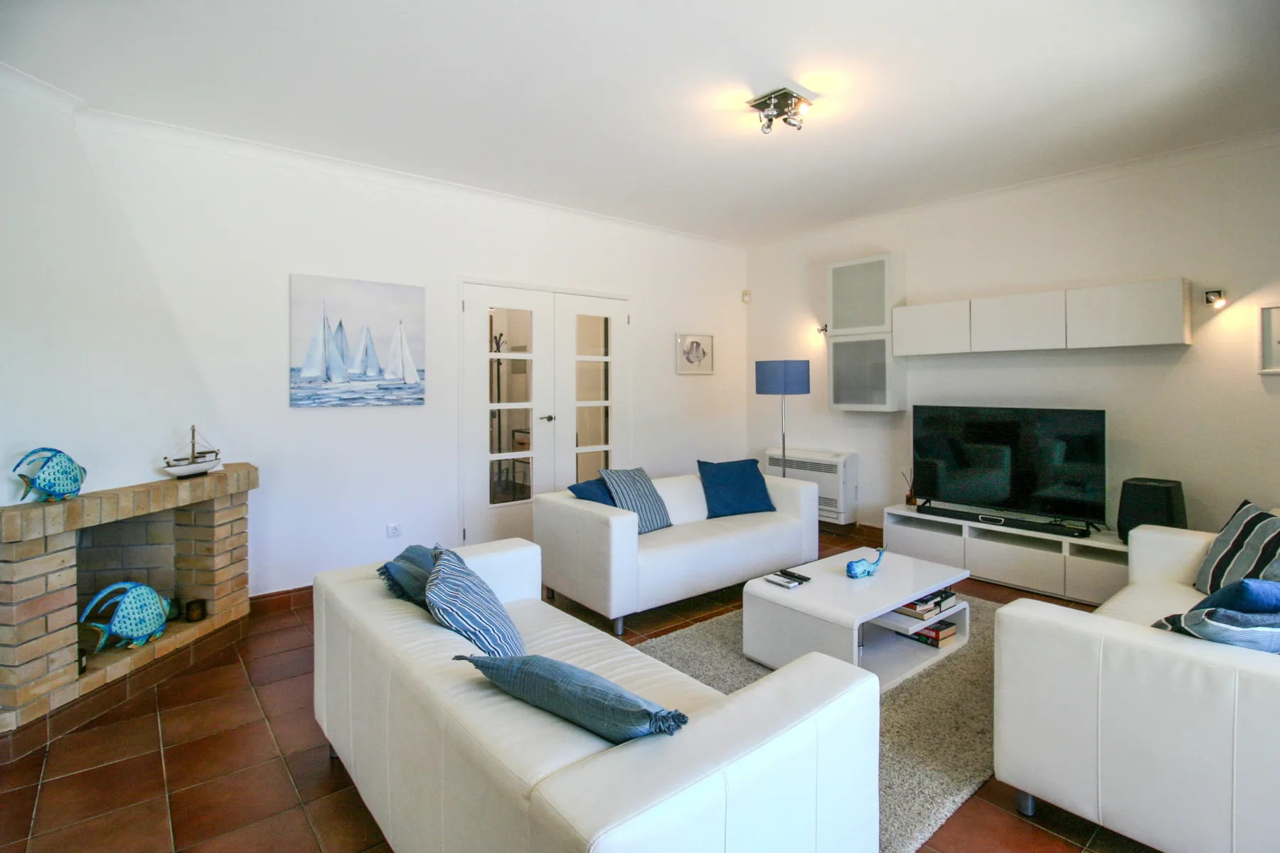 A bright living room with white seating, a television, and a fireplace.