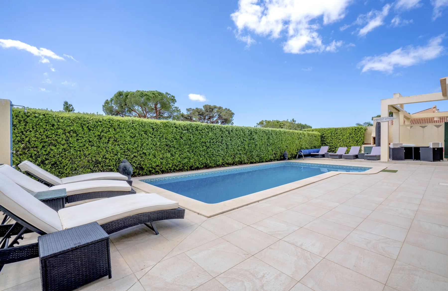 A rectangular swimming pool sits beside a paved patio with reclining seating.