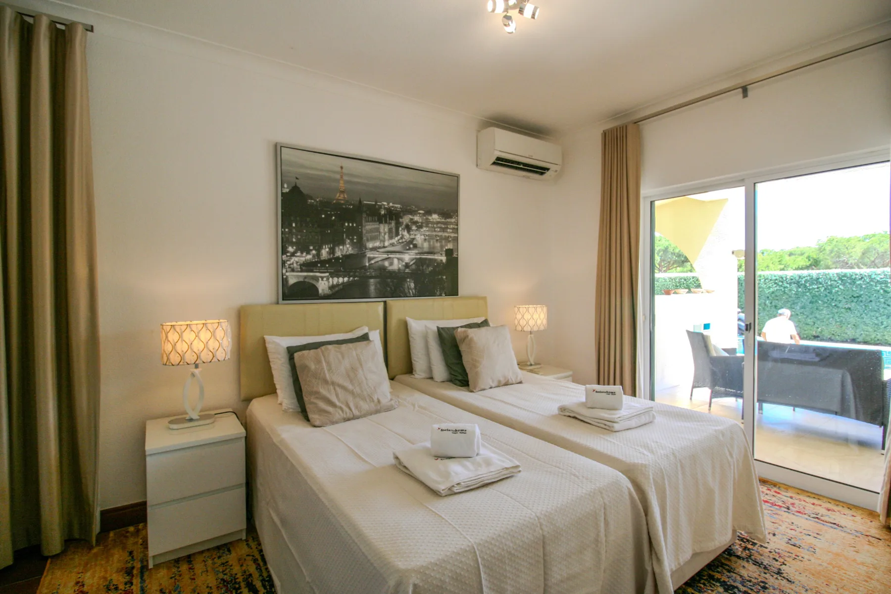 A bedroom with two beds, bedside tables, and a sliding glass door to a balcony.