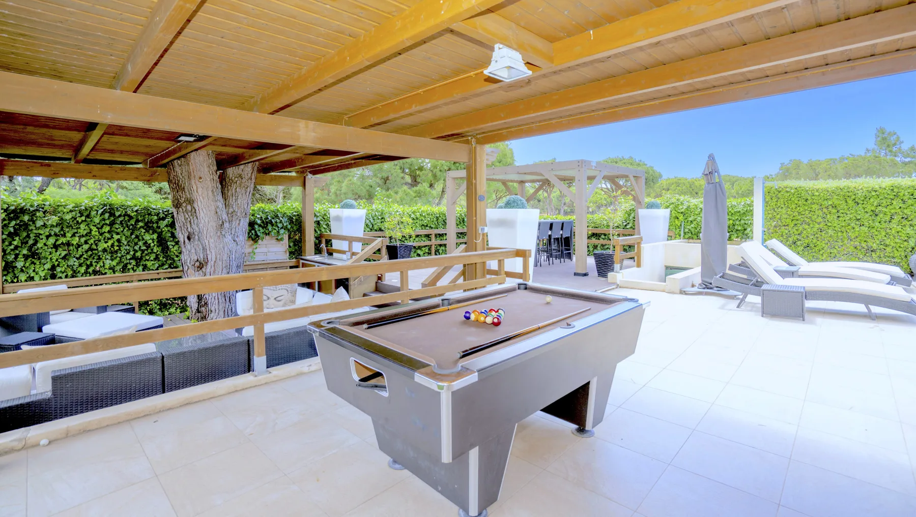 A covered outdoor patio features a pool table, dining seating, and lounge chairs.