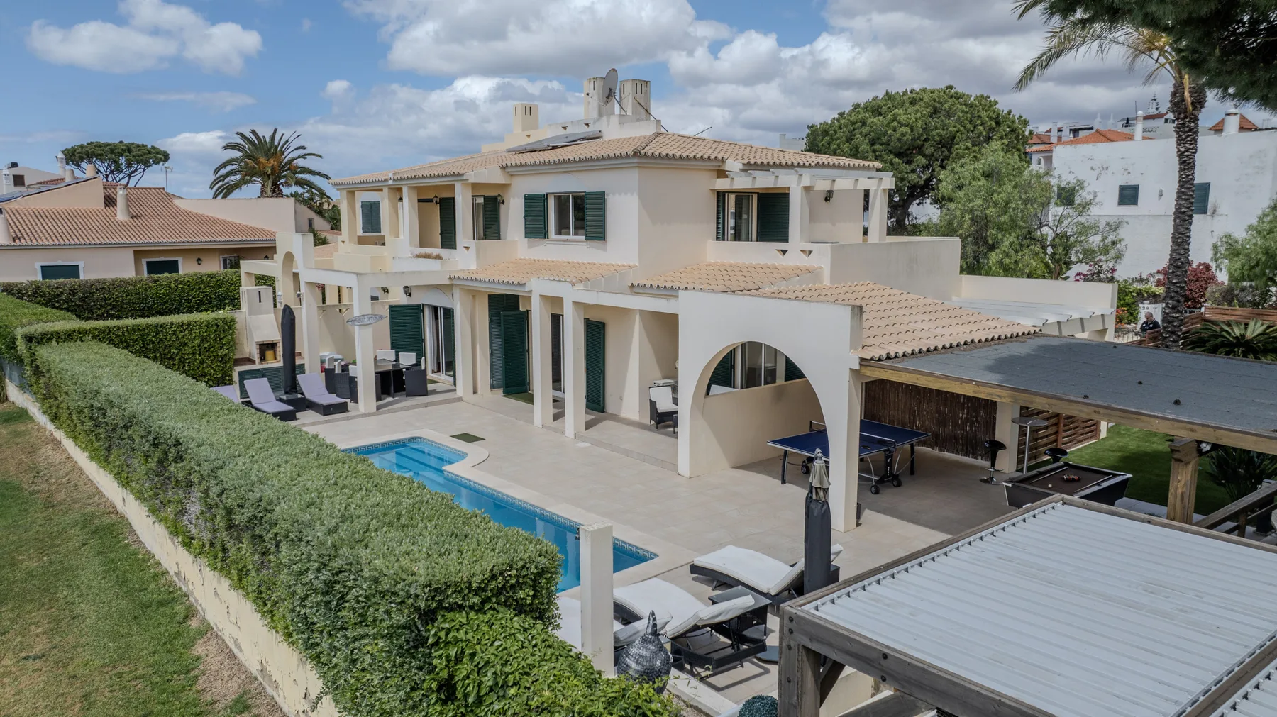 A large villa overlooks a swimming pool, patio seating, and a covered outdoor area.