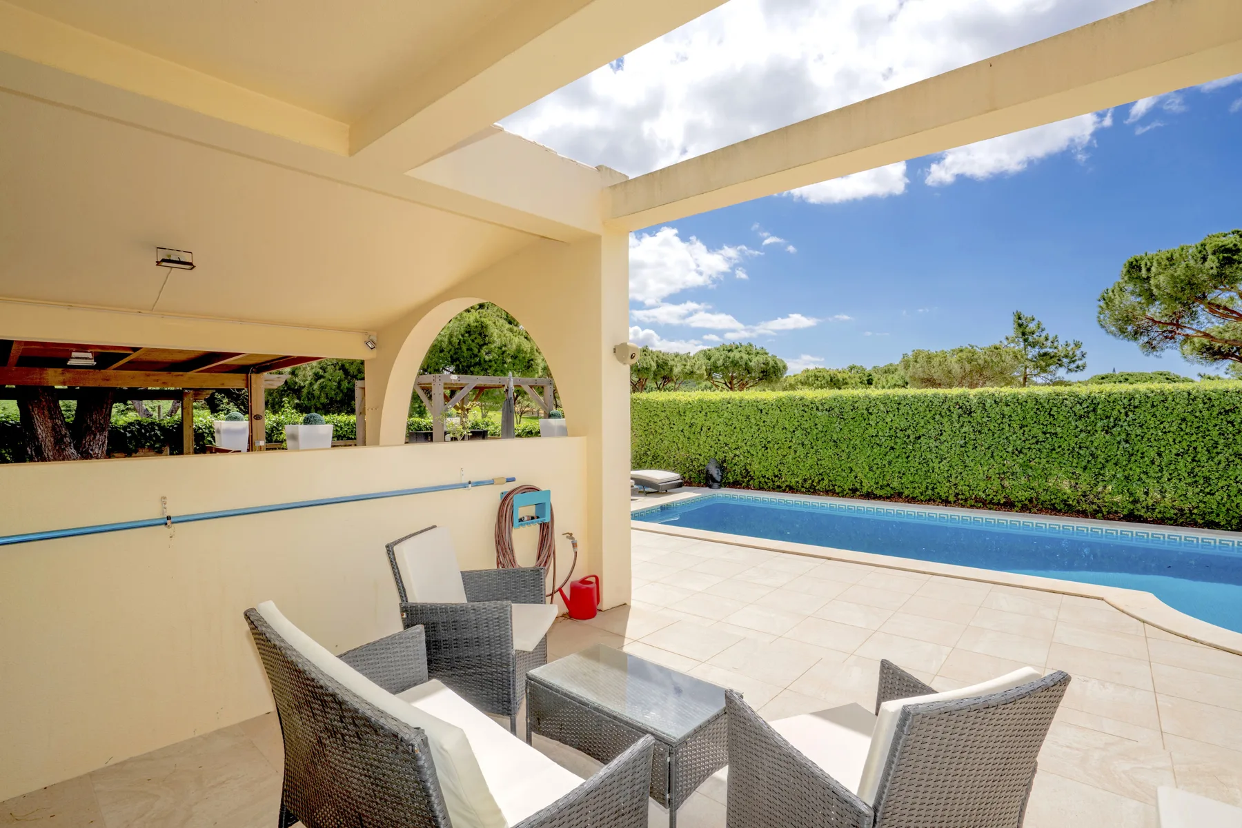 A covered outdoor seating area overlooks a swimming pool and garden.