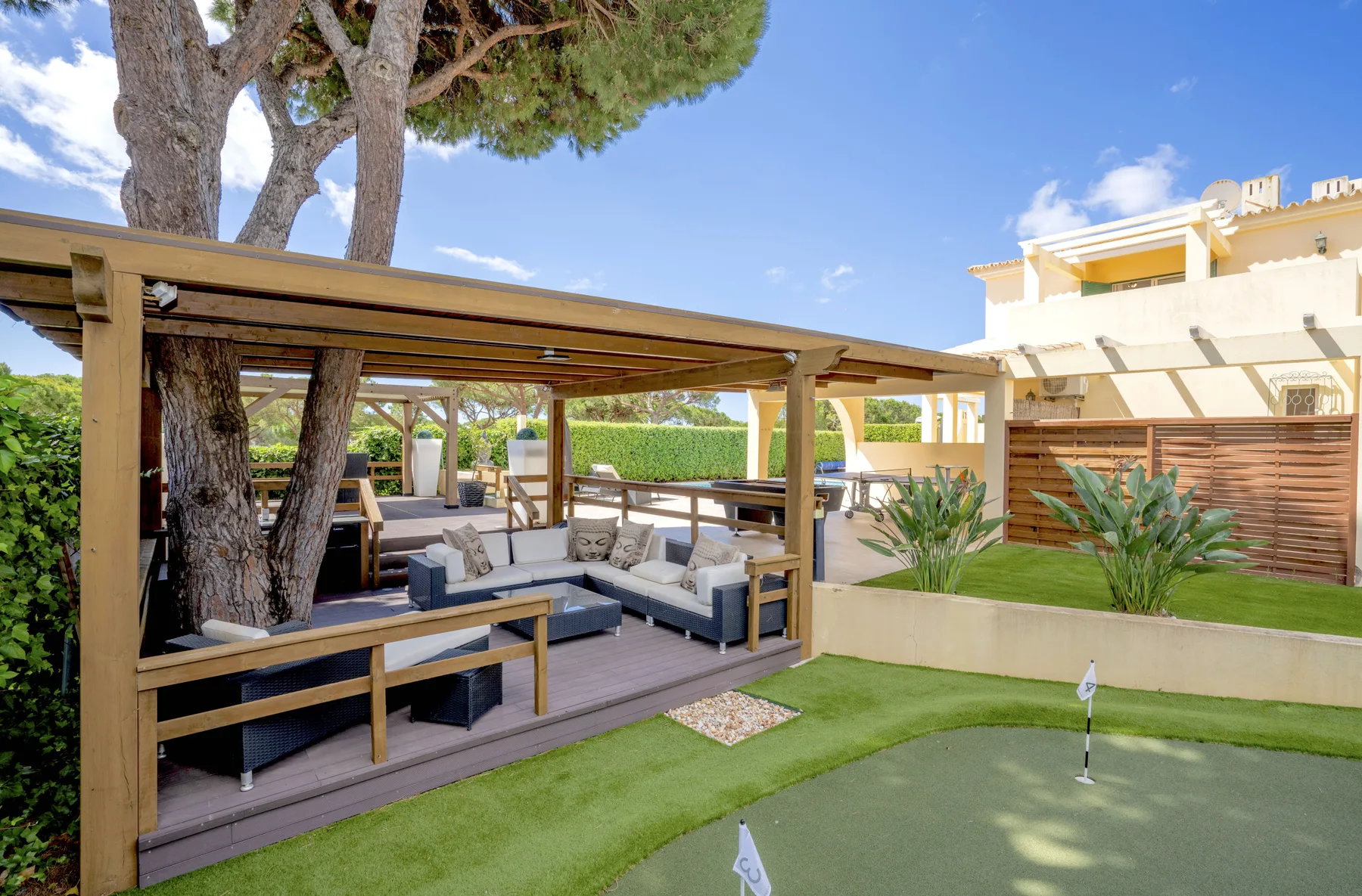 A garden patio has shaded seating beside a small putting green.