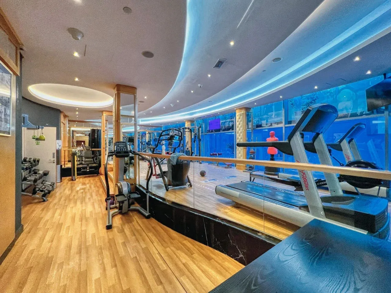 Un gimnasio con cintas de correr y equipos de ejercicio sobre una plataforma con suelo de madera.