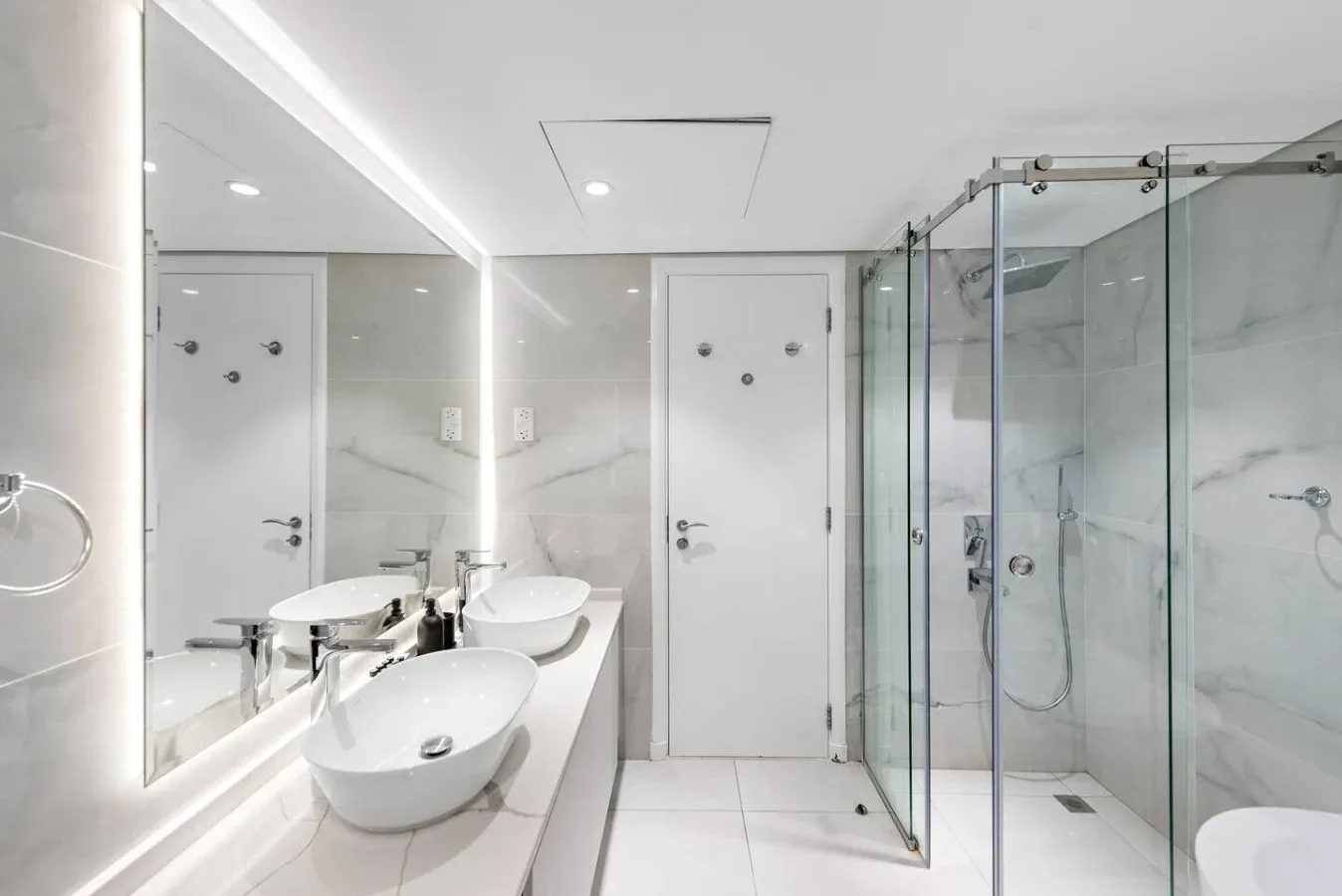 Un baño luminoso con un espejo amplio, lavabos sobre la encimera y una ducha de vidrio.