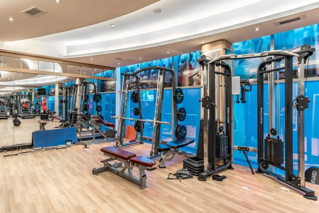 Un gimnasio con máquinas de pesas y bancos junto a paredes con espejos.