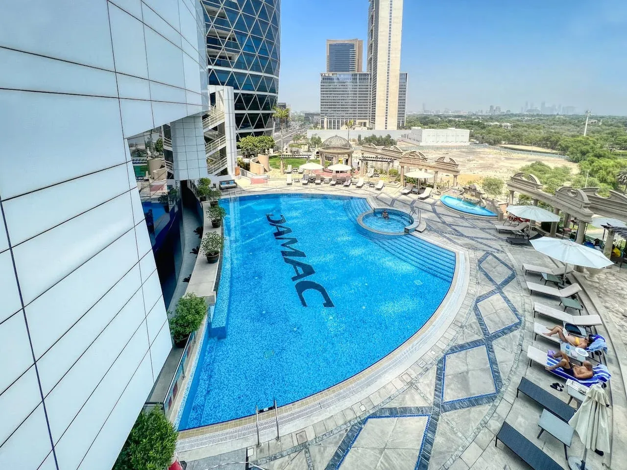 Una piscina en la azotea, con asientos de descanso y edificios de la ciudad al fondo.