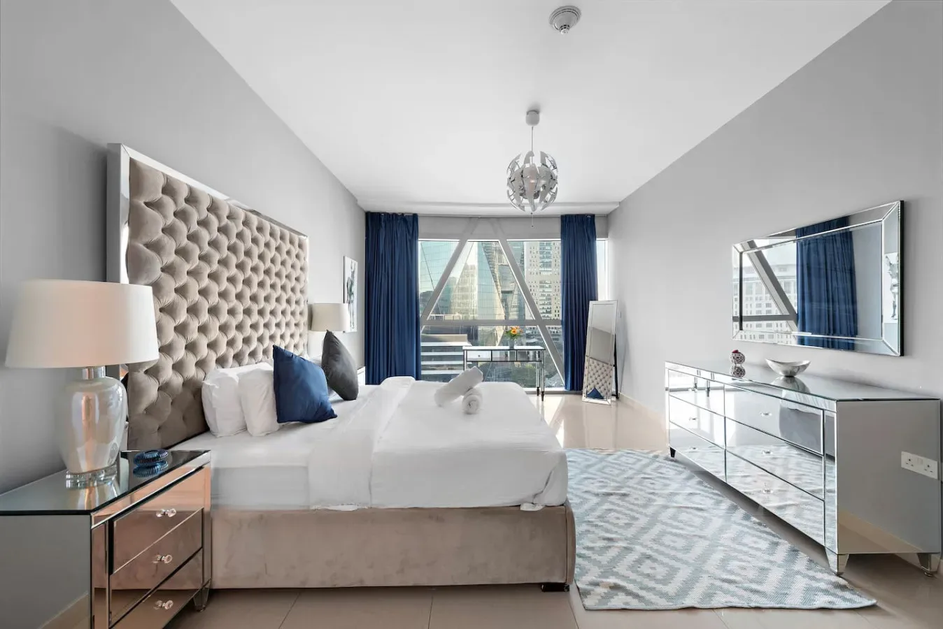Un dormitorio luminoso con una cama grande, cortinas azules y una alfombra estampada.