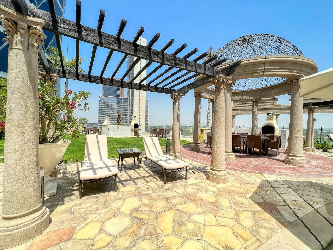 Una terraza exterior soleada con asientos de descanso, una pérgola y un comedor cubierto.