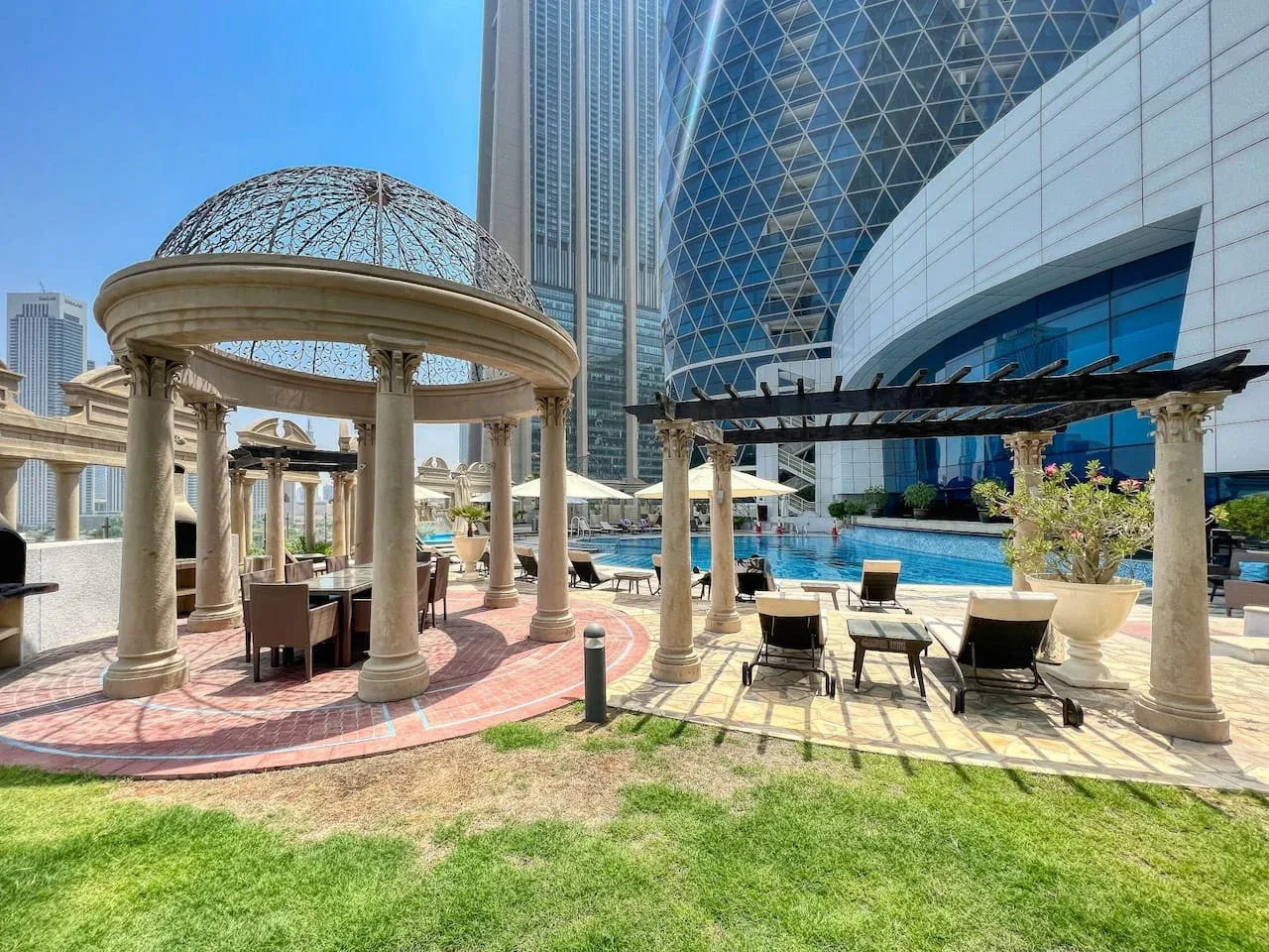 Una zona de piscina al aire libre ajardinada tiene una pérgola circular y asientos.