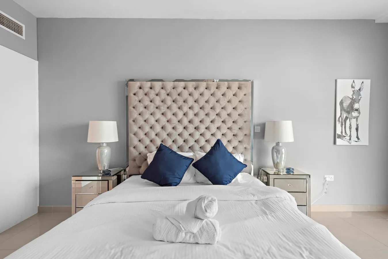 Un dormitorio con una cama bien tendida, almohadas azules y lámparas a ambos lados.