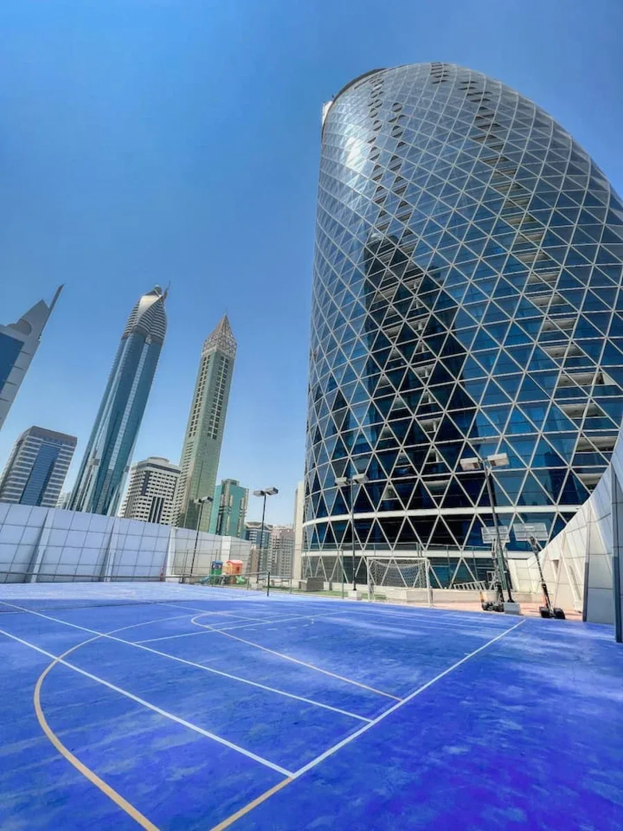 Una cancha deportiva azul al aire libre se encuentra frente a varios edificios altos modernos.