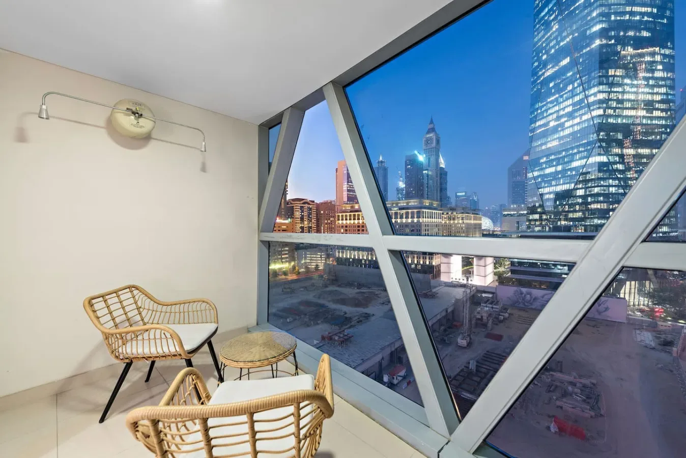 A seating area beside large windows overlooks a city skyline at dusk.