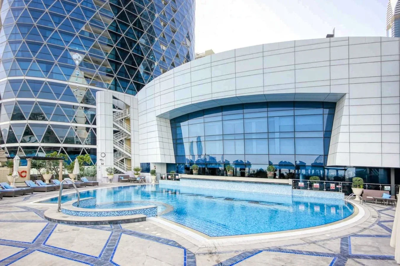 Una piscina al aire libre está junto a edificios modernos de vidrio y color blanco.