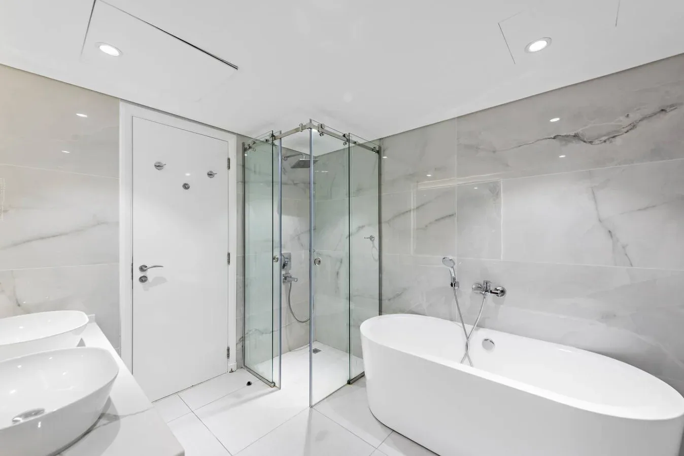 Un baño luminoso con bañera, ducha de vidrio y paredes de azulejos claros.